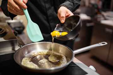 man chef cooking tasty scrambled eggs in frying pan on kitchen
