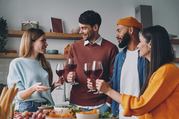 Group of beautiful young people talking and smiling while enjoying dinner at home together
