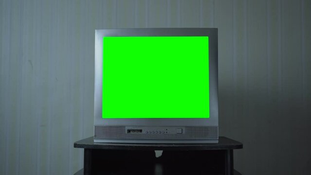 Old analog TV with blank green screen with chroma key with and ability to replace green color with another image stands on wooden nightstand against vintage wallpaper