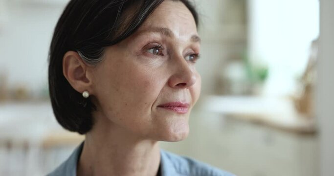 Close up face pensive serious middle-aged woman. Portrait of attractive thoughtful mature female standing at home alone staring into distance looks deep in thoughts, having nostalgic, melancholic mood