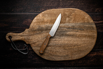 A large wooden cutting board with a knife on a dark wooden table.