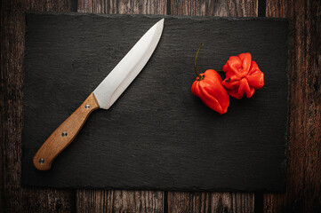 Red hot chili Habanero peppers on a slate cutting board on a dark wooden table with a knife. Top down overhead view.