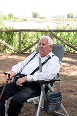 Fototapeta premium 90-year-old grandfather happy in the countryside with family sitting in his chair, with his cane looking at the camera