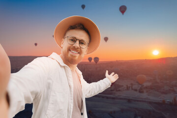 Traveler man taking selfie portrait on background hot air balloons in Goreme Cappadocia Turkey travel