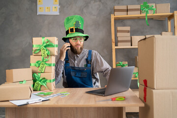 A salesman in a leprechaun hat takes an order by smartphone while sitting in an office with boxes...