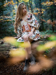 Blonde petite woman with long natural hair sitting on a fallen tree trunk in a mystical forest.