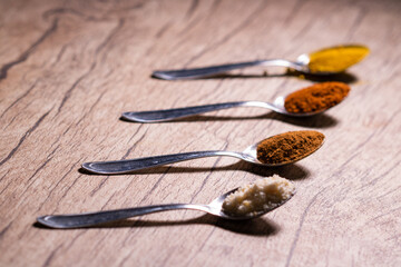 Almonds, cinnamon, paprika and turmeric powder in a spoon on a rustic wooden table.