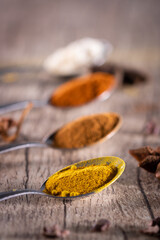 Almonds, cinnamon, paprika and turmeric powder in a spoon on a rustic wooden table.