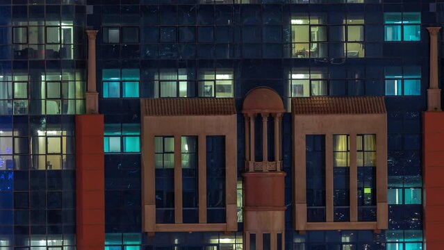 Night aerial view of apartment building glass window facade with illuminated lighted workspace rooms timelapse. Glowing light in skyscraper