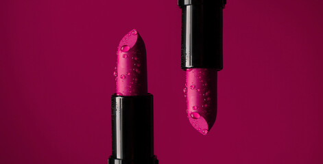 close-up on two red lipsticks in splashes of water on a red background