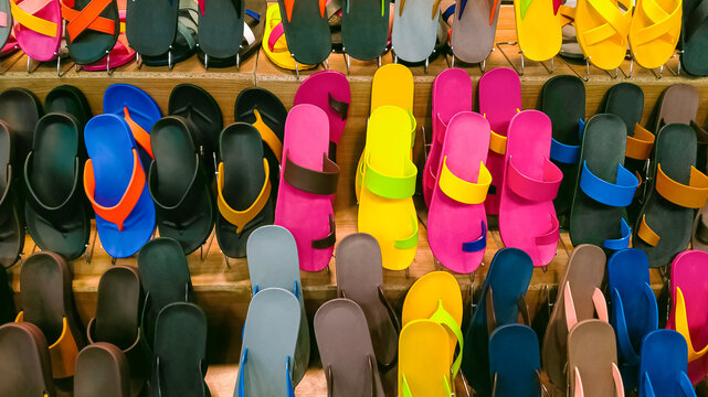 Rows of multicolored rubber sandals and flip flops on wooden shelf display for sale in shopping mall
