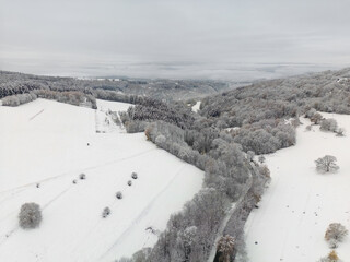 Aerial view of a winding road into a valley with snow covered hills and trees