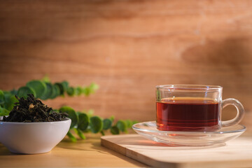 Cup of freshly brewed black tea on wooden board with dried tea leaves in background.