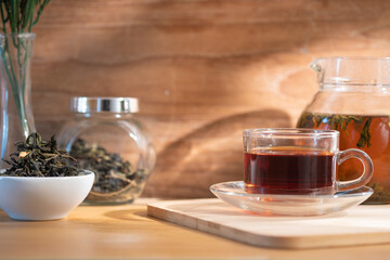 A cup of freshly brewed black tea and dried tea leaves on wooden table with warm soft light.