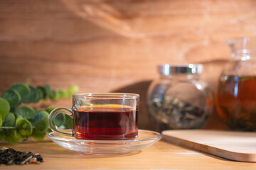 Glass cup of hot aromatic tea with teapot and dried tea leaves on background.