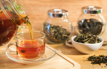 Pouring black tea into pouring from the kettle into a glasses cup.