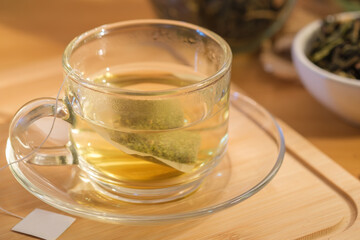 A glass cup of healthy herbal tea with tea bag on wooden board.