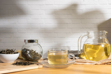 Cup of hot brewed tea, teapot and dried tea leaves on wooden table  with soft sunlight shining.