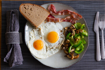 Traditional English breakfast plate with two fried eggs bacon slices, green peppers, mushrooms and bread toast. Ketogenic diet concept