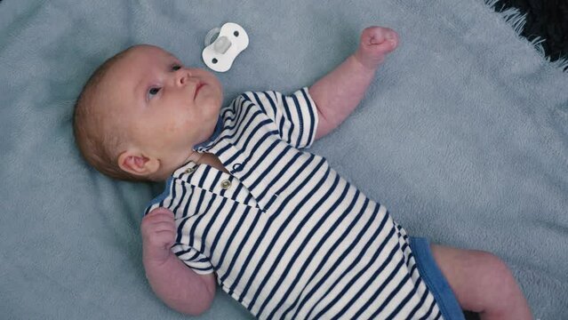 Newborn infant lying on his back on a gray blanket. The little girl woke up in the room of the house