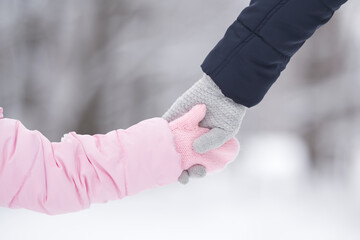 Little daughter and young adult mother holding each other hands in warm gloves on nature background. Walking and spending time together in cold winter day. Closeup. Back view.