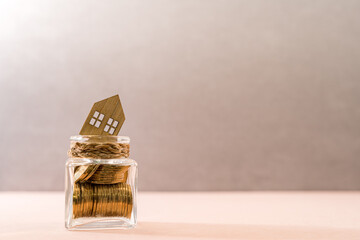 Bottle with gold coin inside and house model put on the top on the desk in the office, Saving money or loan for business investment real estate or buy a new home for a family concept.