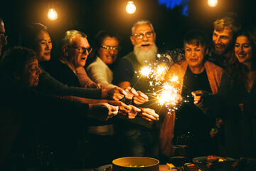 Happy family celebrating with sparkler fireworks on new year's eve - Focus on left senior woman hand