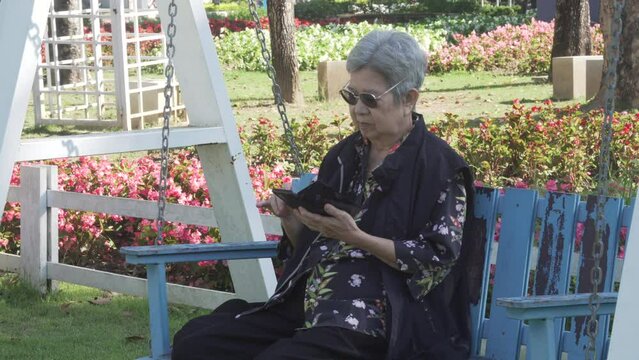 asian old elder senior woman elderly using social media on mobile smart phone cellphone in garden. mature retirement lifestyle