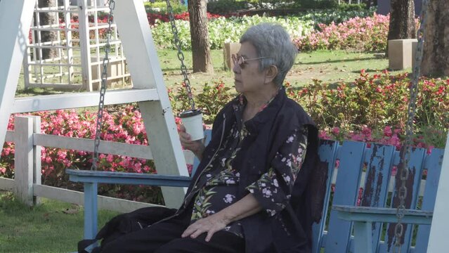 old elderly elder senior woman drinking coffee relaxing in flower garden park