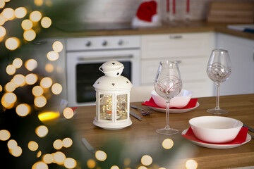 Selective focus on Beautiful table setting for Christmas dinner with transparent glasses and porcelain plates against the background of a Christmas tree and bokeh lights. Blurred background