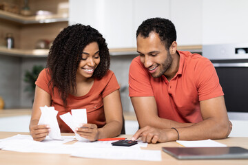 Smiling millennial black couple in red t-shirts work with documents, calculate profit, check bills in kitchen interior