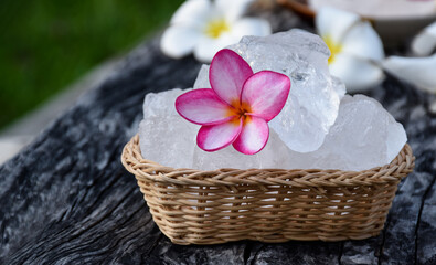 Soft focus of purple plumeria flower and white alum cube on wicker basket, spa and skincare concept.
