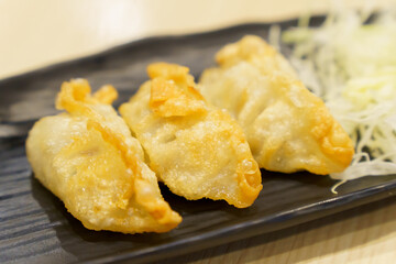 Close-up of golden yellow gyoza placed on black plate with blurred background