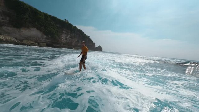 Man surfer riding pumping on sea ocean wave on shirt surfboard extreme sport hobby lifestyle leisure aerial view. Male surfing sunlight paradise tropical resort cinematic sky landscape FPV drone shot