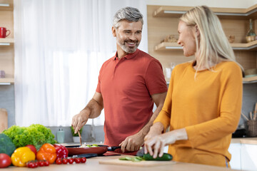 Happy middle aged spouses cooking and having conversation, kitchen interior