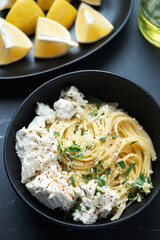 Middle close-up of spaghetti with ricotta cheese and lemon zest in a black bowl, vertical shot, selective focus