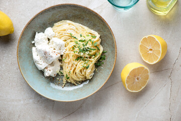 Rustic plate with lemon and ricotta spaghetti on a beige stone background, horizontal shot, top view