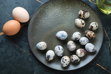Dark-olive plate with raw quail eggs, above view on a dark-olive marble background, horizontal shot