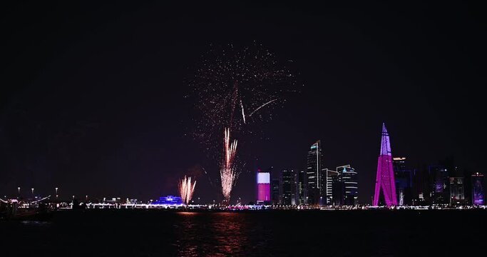 Coloful celebration fireworks and illuminated skyscraper skyline of Doha at night in Qatar, Middle East against dark sky. Visible advertisements on skyscraper buildings from football world cup