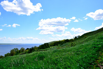 slope of the hill covered with green grass and blue sky and white clouds on background