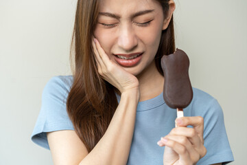 Face expression suffering from sensitive teeth and cold, asian young woman, girl feeling hurt, pain eating ice cream, lolly. Toothache molar tooth at home, dental problem isolated on white background. - obrazy, fototapety, plakaty