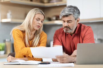 Concerned middle aged spouses working on family budget, kitchen interior