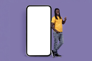 Positive african american young man posing by huge smartphone, mockup