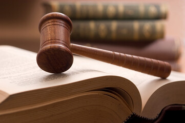 Court gavel resting on law book and other books are seen behind..