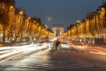 Paris - France,France - 12 08 2022: View of the Arc-De-Triomphe and Avenue des Champs Elysees with Christmas lights and full moon - obrazy, fototapety, plakaty