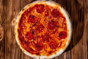 Pizza with tomato sauce, mozzarella, salami, chili, honey on wood background. View from above