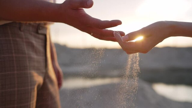 Male and female hands pour sand. The hands of a young girl and a guy pour sand from the beach at sunset. Sand out of your hands. - Powered by Adobe