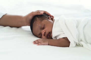 Obraz na płótnie Canvas Portrait of Infant Black African American sleeping on white bed with mother hand in bedroom. During Daytime Sleep At Home. Newborn baby health care concept.