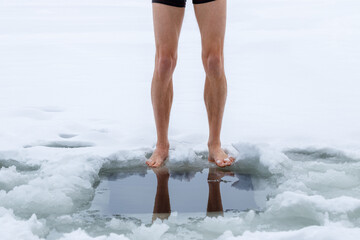 Winter hardening in cold water. Men's legs and a hole close-up.