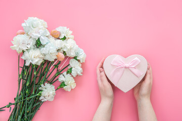 A bouquet of flowers and a gift box in female hands on a pink background.